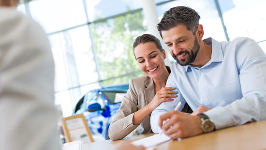 A young couple signing paperwork for a new car